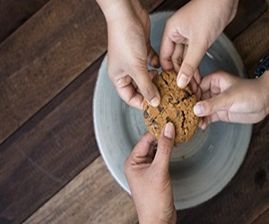 Ein Keks, den vier Händen halten, über einem Teller