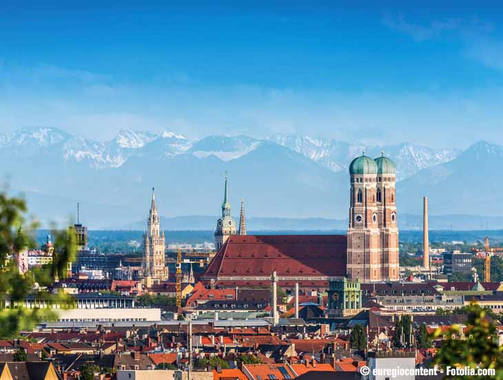 Im Vordergrund München mit Frauenkirche, im Hintergrund Berge.