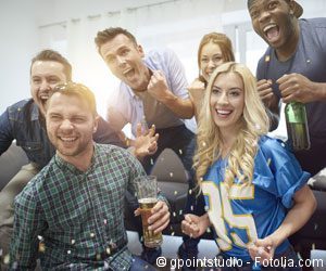 Männer und Frauen jubeln vor dem Fernseher mit Bier in der Hand