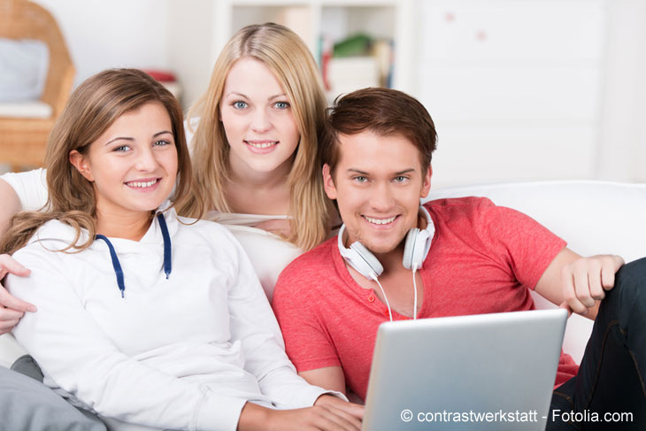 A young man and two young women sitting on a sofa with a laptop