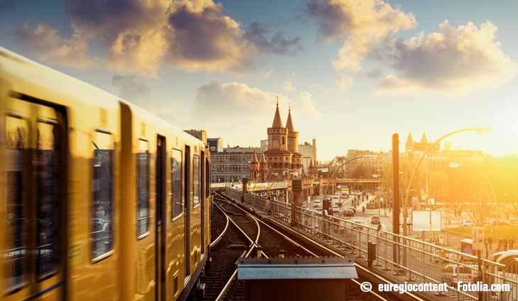 Links sieht man die gelbe Berliner U-Bahn wie sie über eine Brücke in Richtung Stadt und Abendsonne fährt.