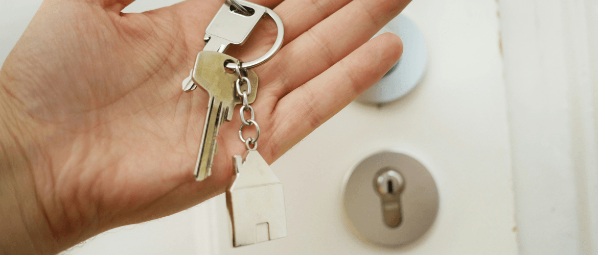 Hand hält Wohnungsschlüssel mit Hausanhänger – Symbol für temporäre Vermietung und Wohnen auf Zeit.