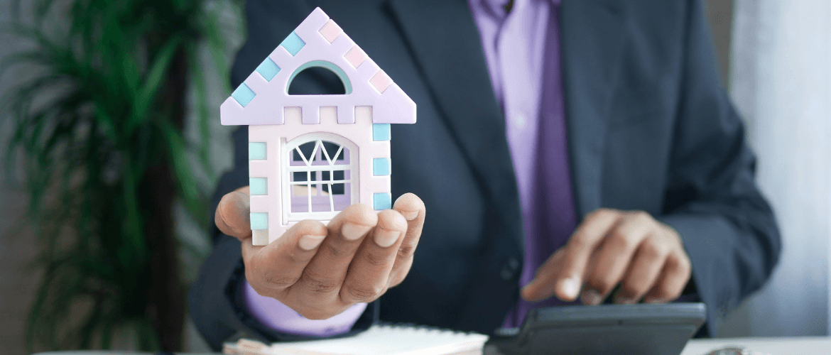 Mann im Anzug hält Modellhaus und tippt auf Taschenrechner – Symbol für professionelle Immobilienvermietung.