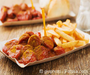 Currywurst mit Pommes in einer Pappschale.