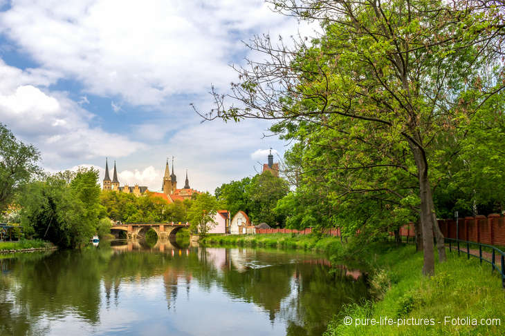 There is a river and a bridge. In the background there is are steeples.