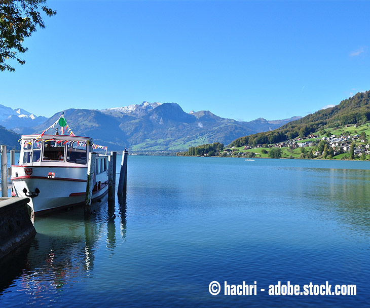 Ein kleines Schiff auf dem Sarnersee mit blauem Himmel und Bergen im Hintergrund.